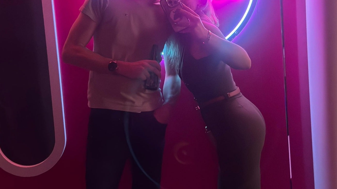 Twee mensen een man en een vrouw maken een selfie in een ruimte met roze neonverlichting.