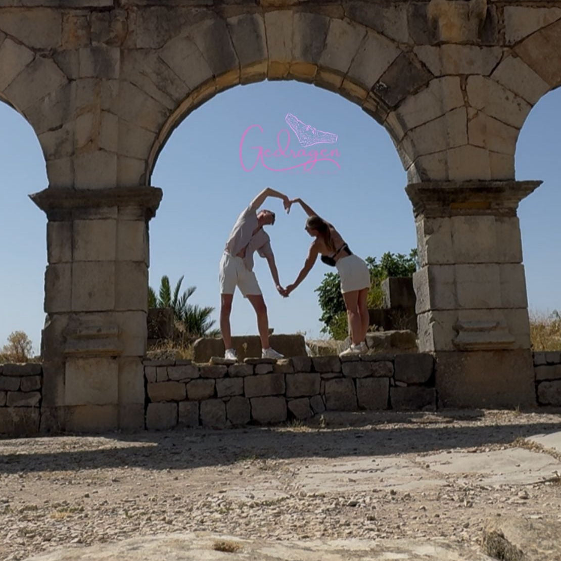 Romantisch stel maakt samen een hartvorm met hun armen onder een oude stenen boog, symbolisch beeld van liefde en verbondenheid.